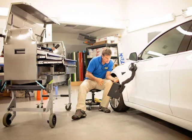 Dent King technician performing paintless dent repair on a white car using a specialized PDR light and professional tool cart in the workshop