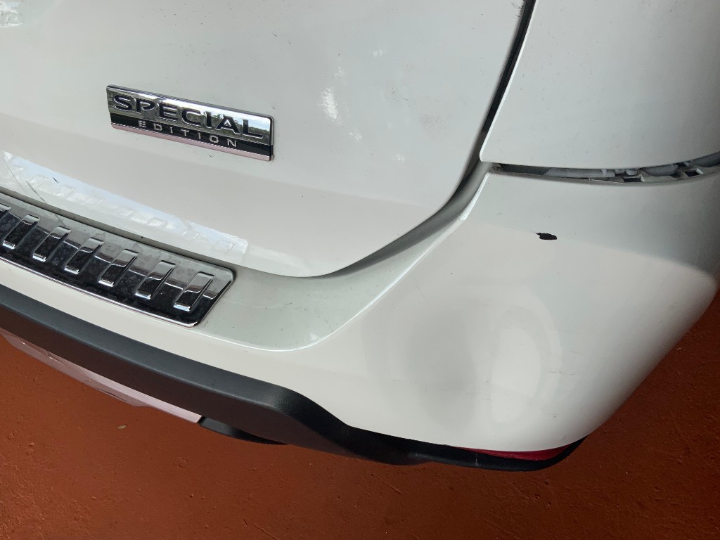 Large dent on a white car rear bumper with panel misalignment