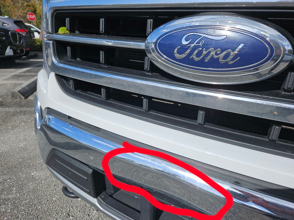 Dent on a chrome Ford front bumper highlighted near the grille
