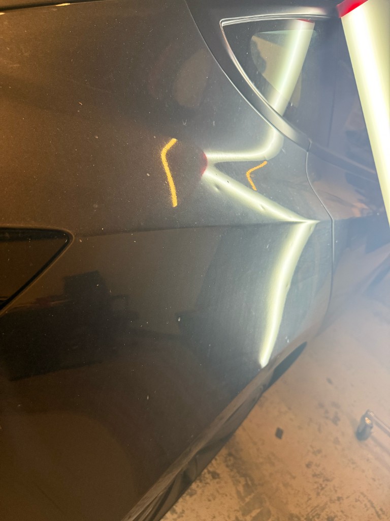 Door dings on a dark car panel highlighted with PDR inspection lights