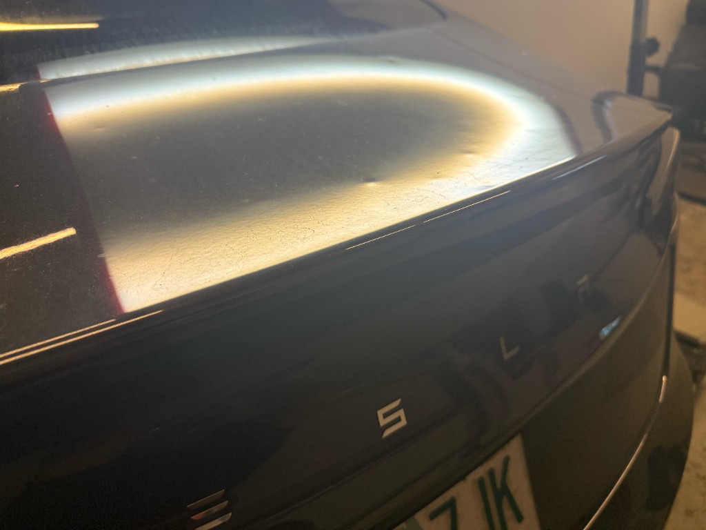 Small ding on a Tesla trunk lid highlighted in the light reflection