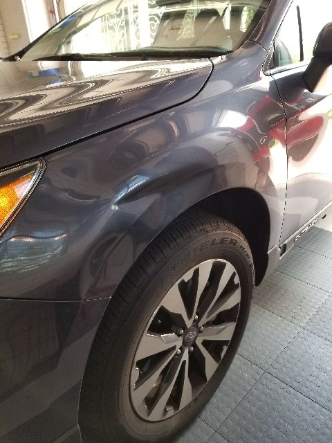 Large deep dent on a dark SUV front fender above the wheel arch