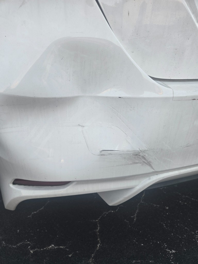 Large dent and scuffing on a white car rear bumper