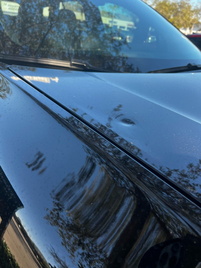 Medium dent example on a black car hood near the fender