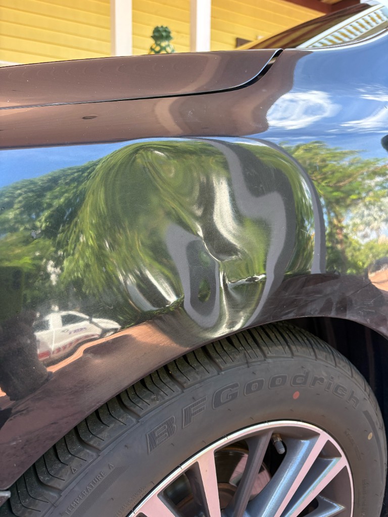 Scratches and paint damage on a dark car fender near the front wheel