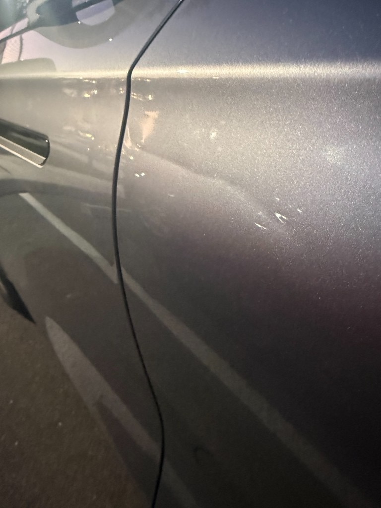 Horizontal scratches and paint chips on a dark metallic car door panel