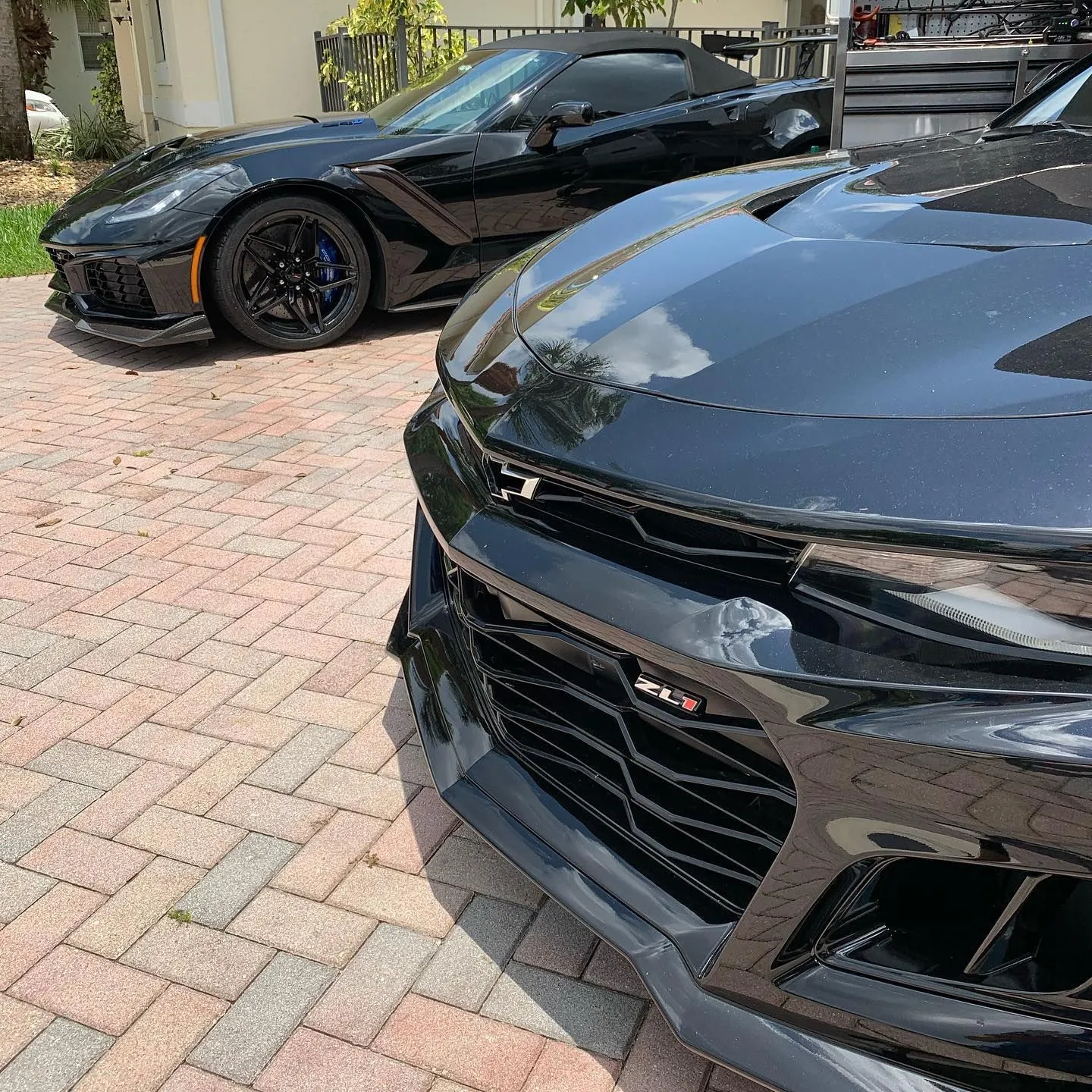 Black Chevrolet Camaro ZL1 and Corvette parked on a brick driveway with flawless reflective paint finish